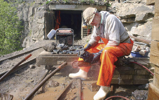 Byron(+) trimming specimens at the mine. Only a miner would sit on a diamond chainsaw to get the best angle for cutting! J. Fisher photo.